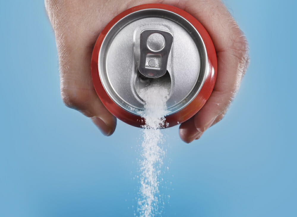 biały cukier wysypuje się z puszki od coca coli